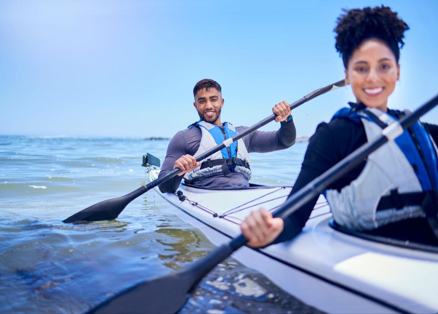 A couple with safety swimming vests smiles at the camera while kayaking.