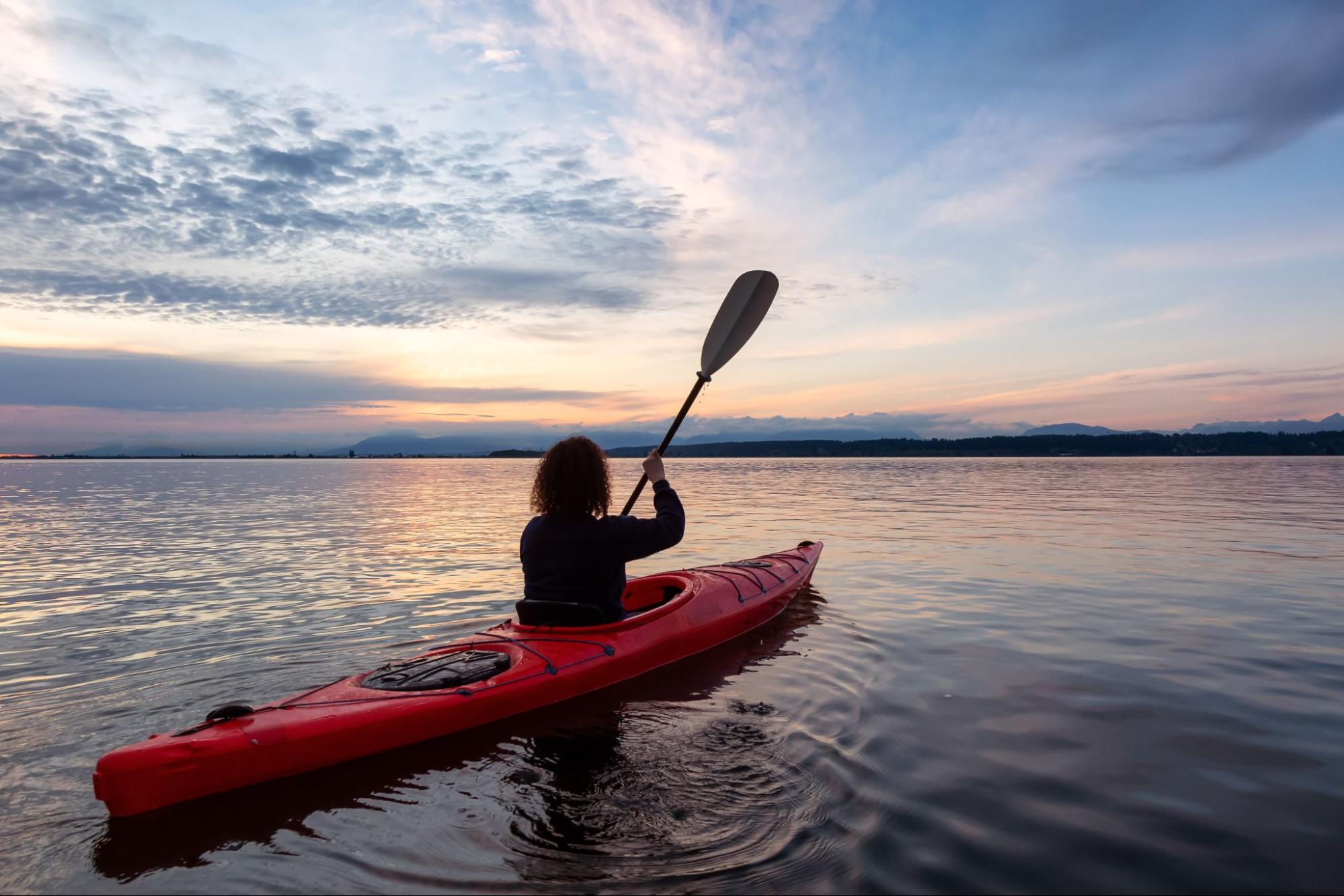 Woman on a kayak with a sunset in the background. 