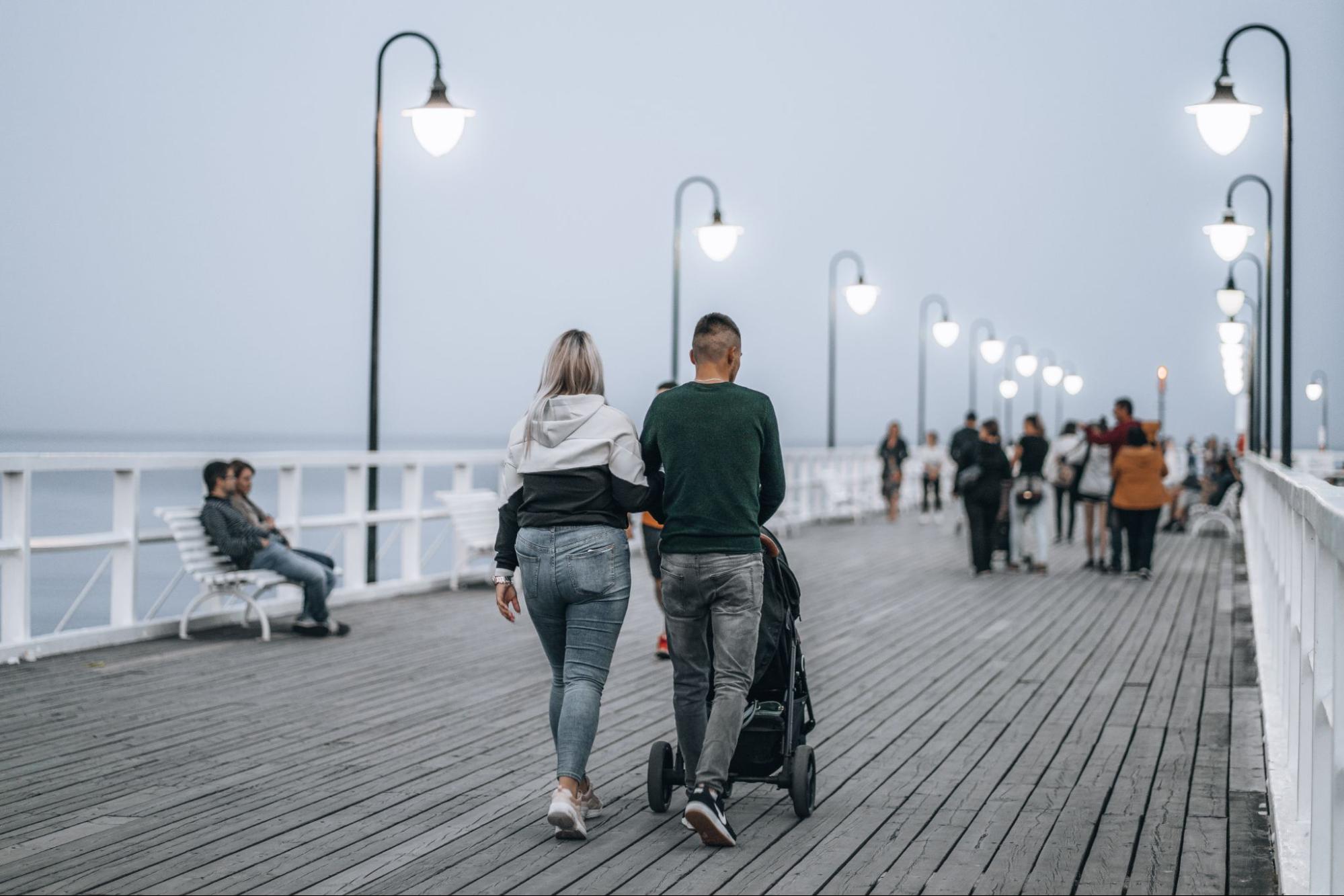 People strolling along a boardwalk illuminated by stylish streetlamps.