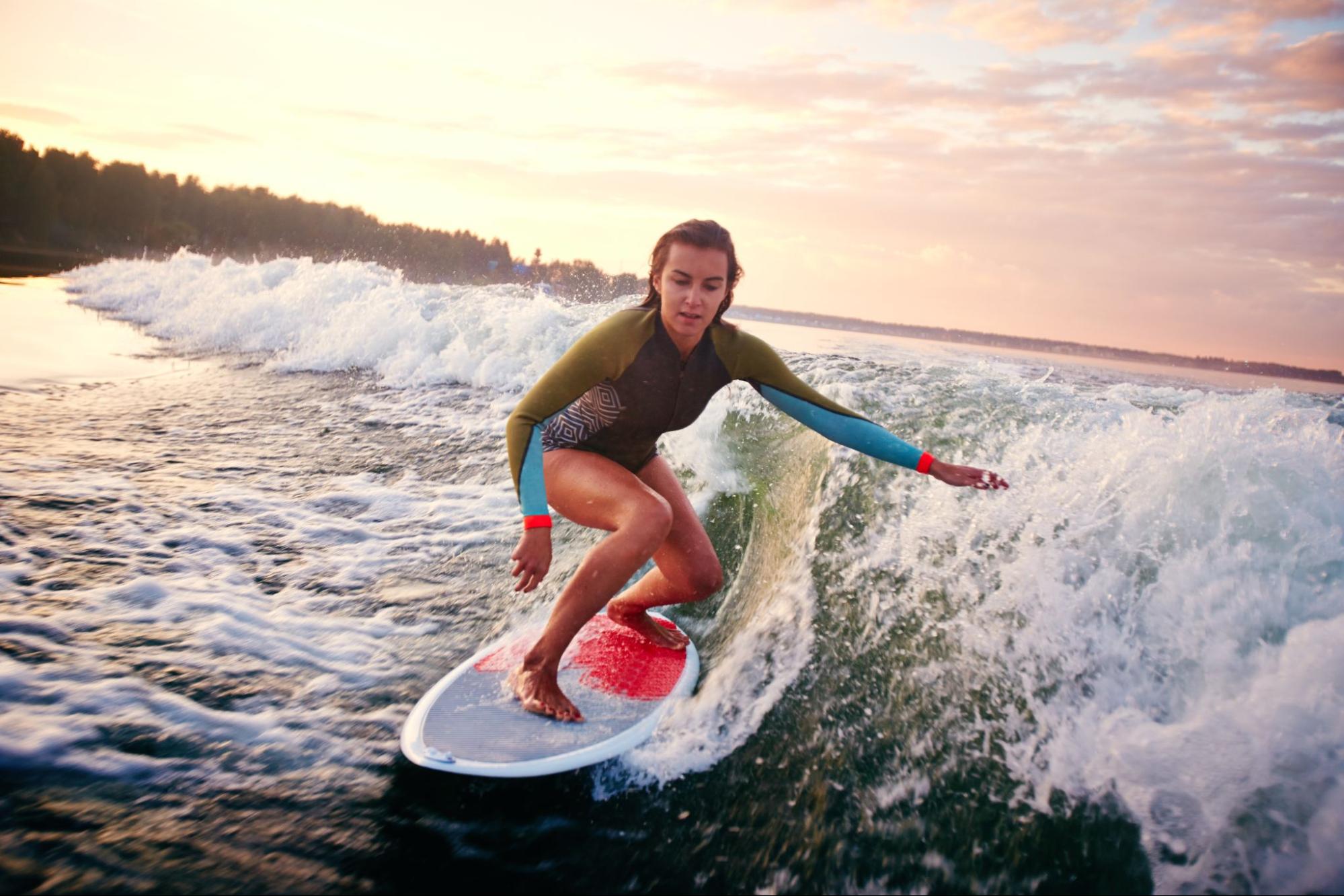 A woman in a rash guard skillfully surfboarding amidst big waves, showcasing her balance and technique.