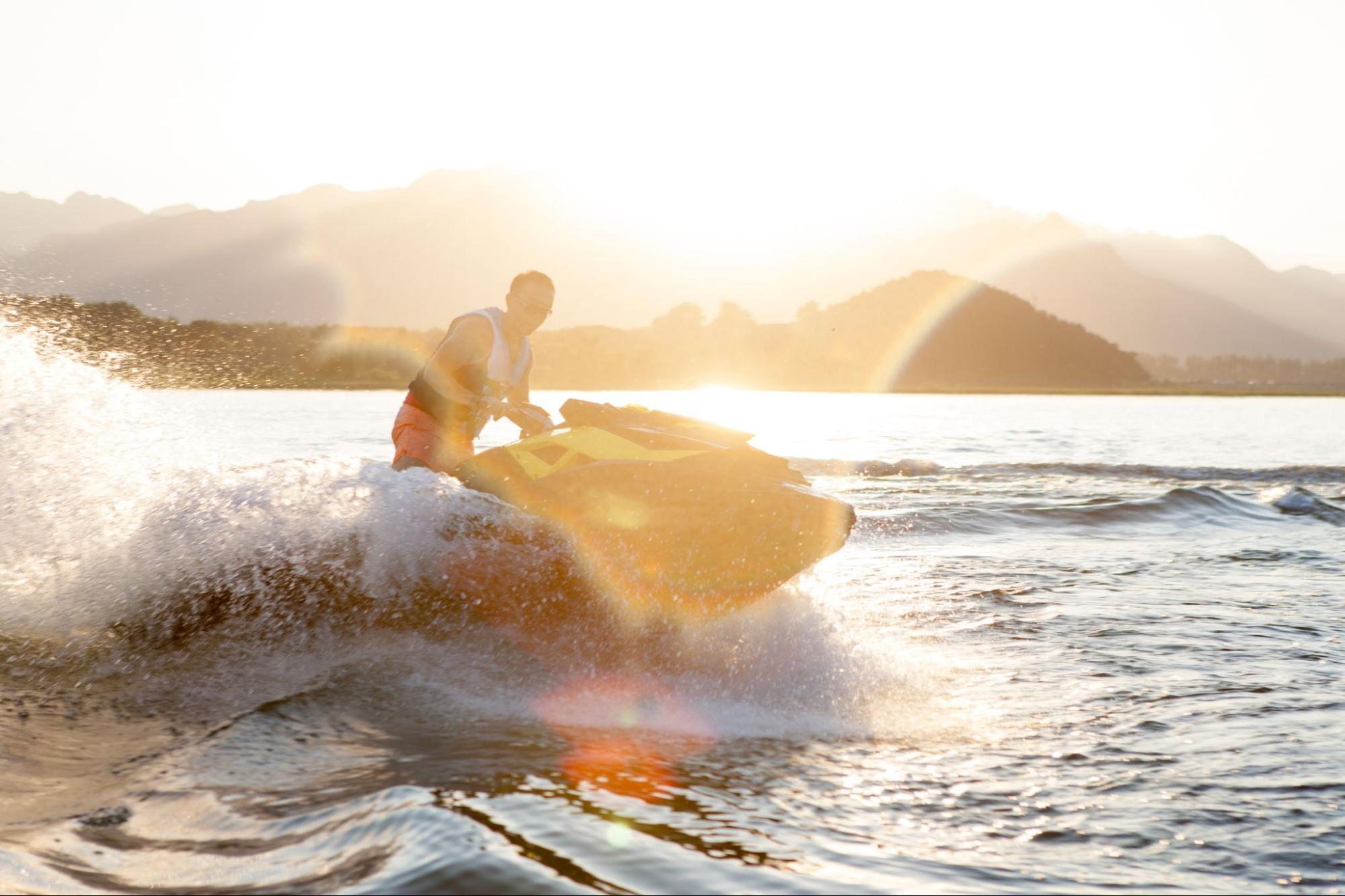 image3 Man on a waverunner with a lifejacket on with the sun and mountains in the background.