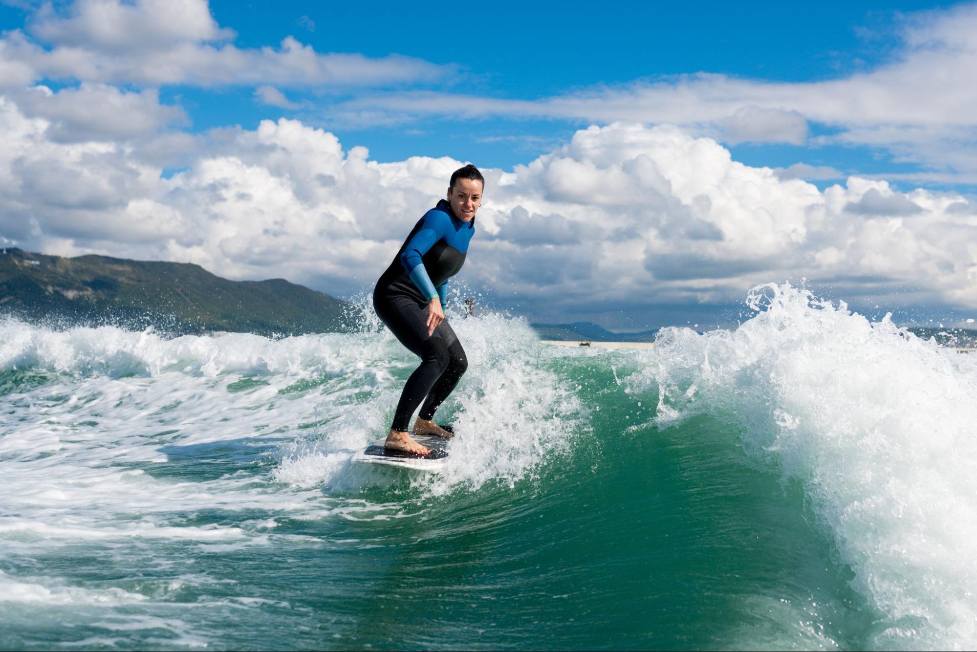 A young athletic woman in a wetsuit surfs on a board, balancing confidently on a wave with focus and energy.